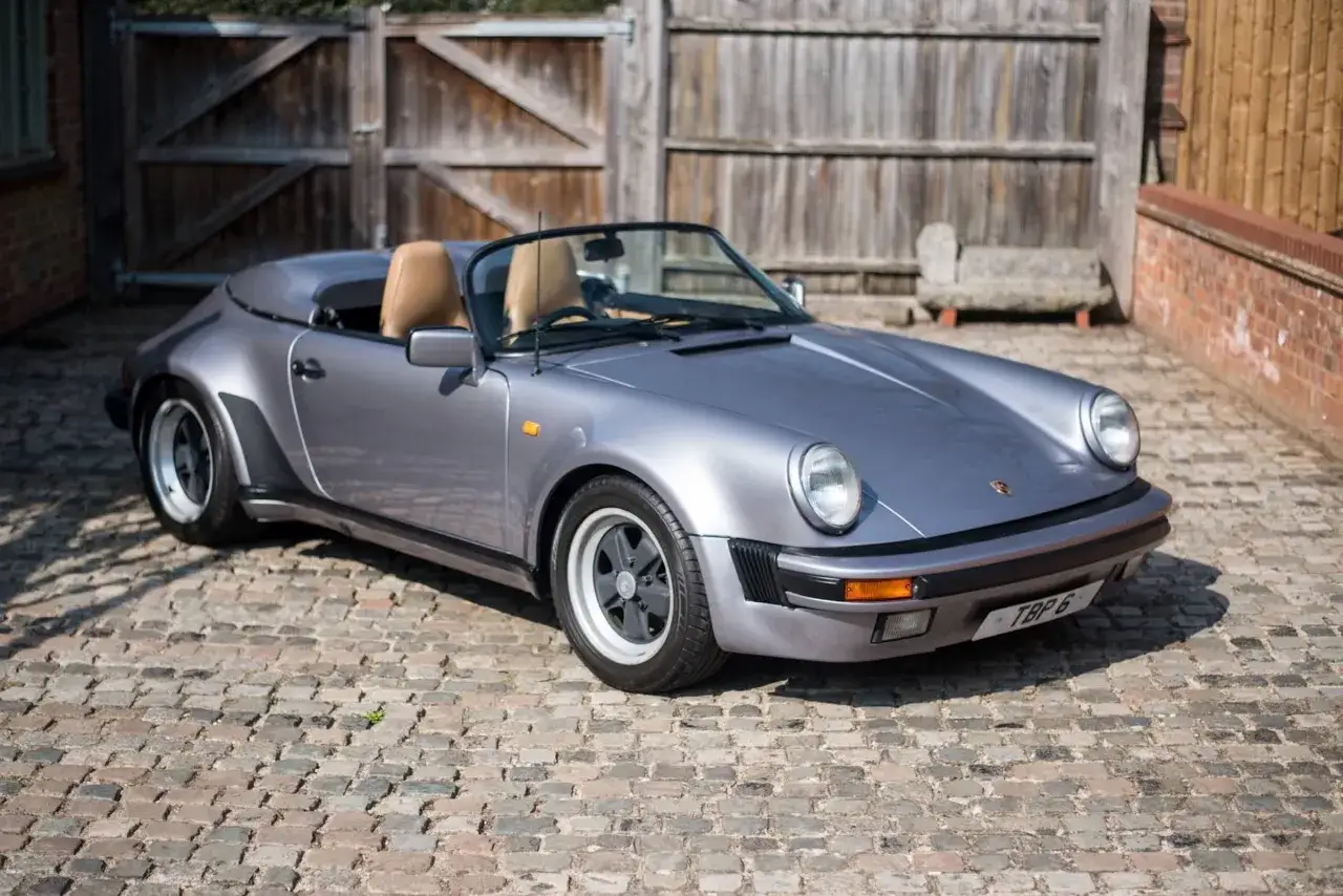 Srebrny Porsche 911 Speedster z beżowym wnętrzem stoi na brukowanym podwórku, gotowy na przejażdżkę.