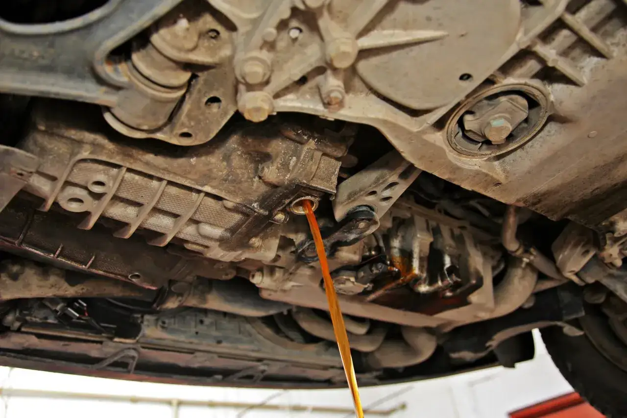 Płynny strumień oleju wypływa z mechanizmu, wskazując na wymianę oleju w skrzyni biegów.