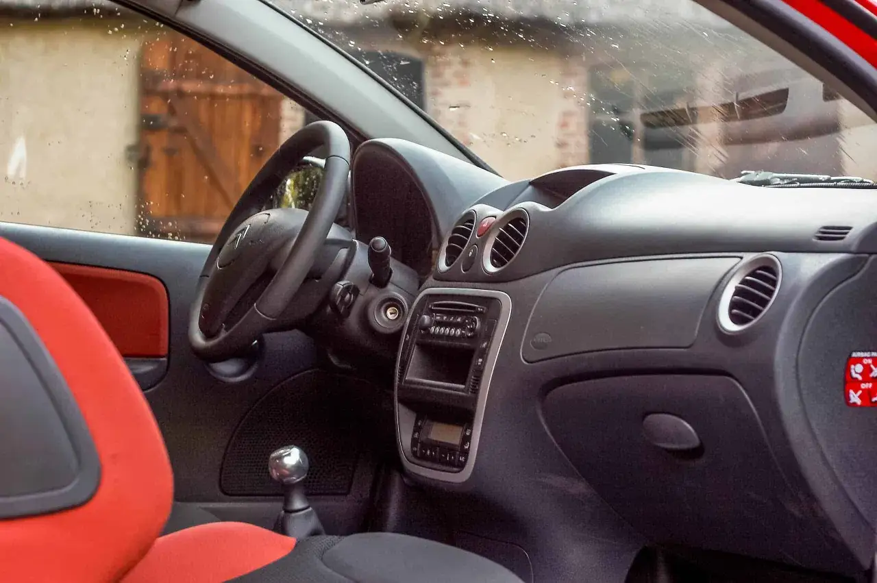 Wnętrze Citroena C2 VTR z czerwonymi akcentami na siedzeniach i czarną deską rozdzielczą. Widoczny fragment kierownicy, dźwigni zmiany biegów i radia.