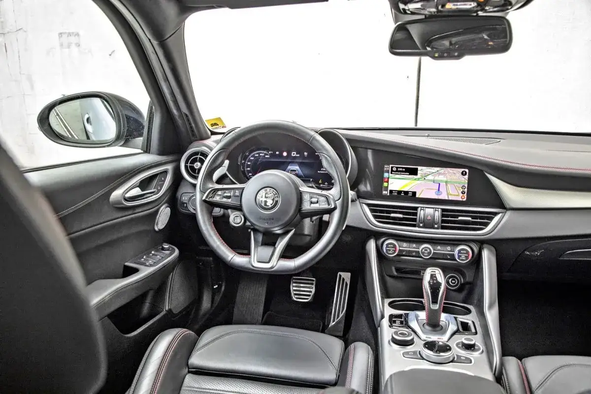 Wnętrze Alfa Romeo Giulia, z kierownicą, ekranem nawigacji i konsolą środkową. Wiele osób chwali ten model, a opinie o Alfa Romeo Giulia są zazwyczaj pozytywne.