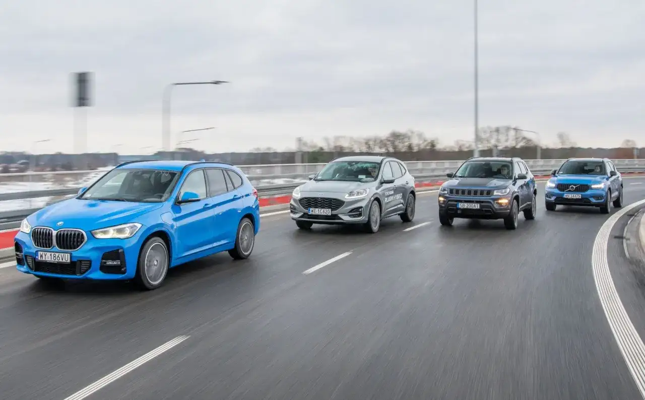 Niebieskie BMW X1, Ford Kuga, Jeep Compass i Volvo XC40 jadą drogą. Wiele osób szuka bmw x1 opinie przed zakupem.