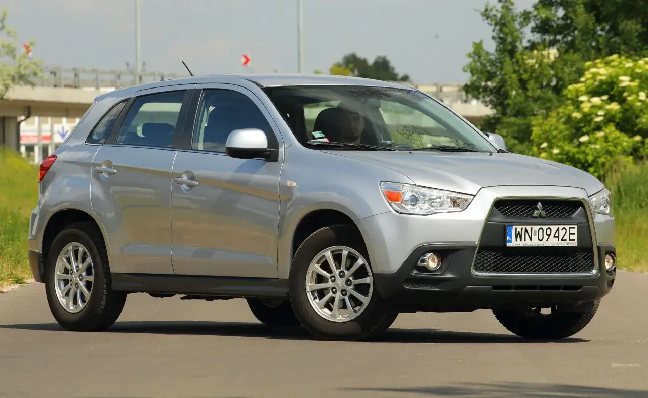 Srebrny Mitsubishi ASX na drodze. Kierowca w środku, za nim zielone drzewa. Wiele pozytywnych mitsubishi asx opinie.