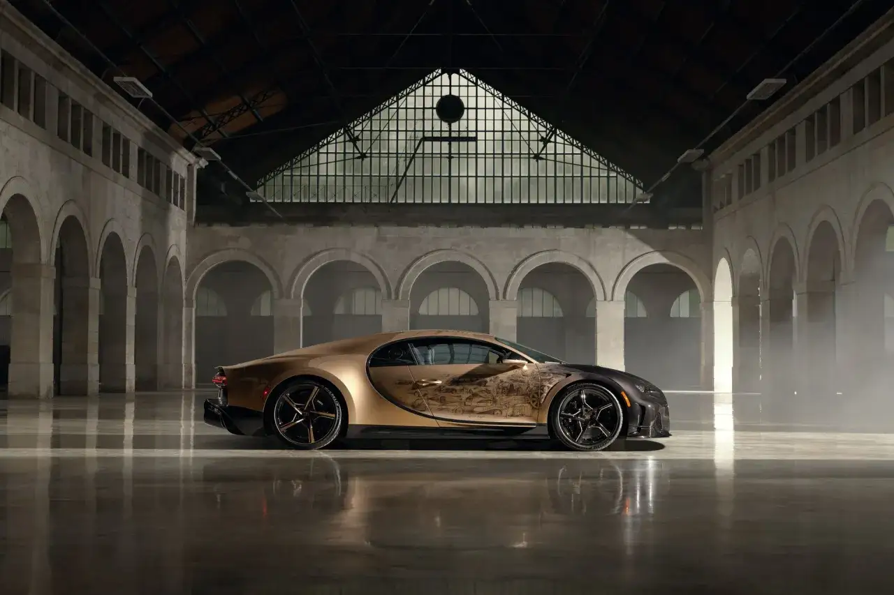 Złoty Bugatti Chiron Super Sport z unikatowym malunkiem historycznych modeli, lśni w industrialnej hali.