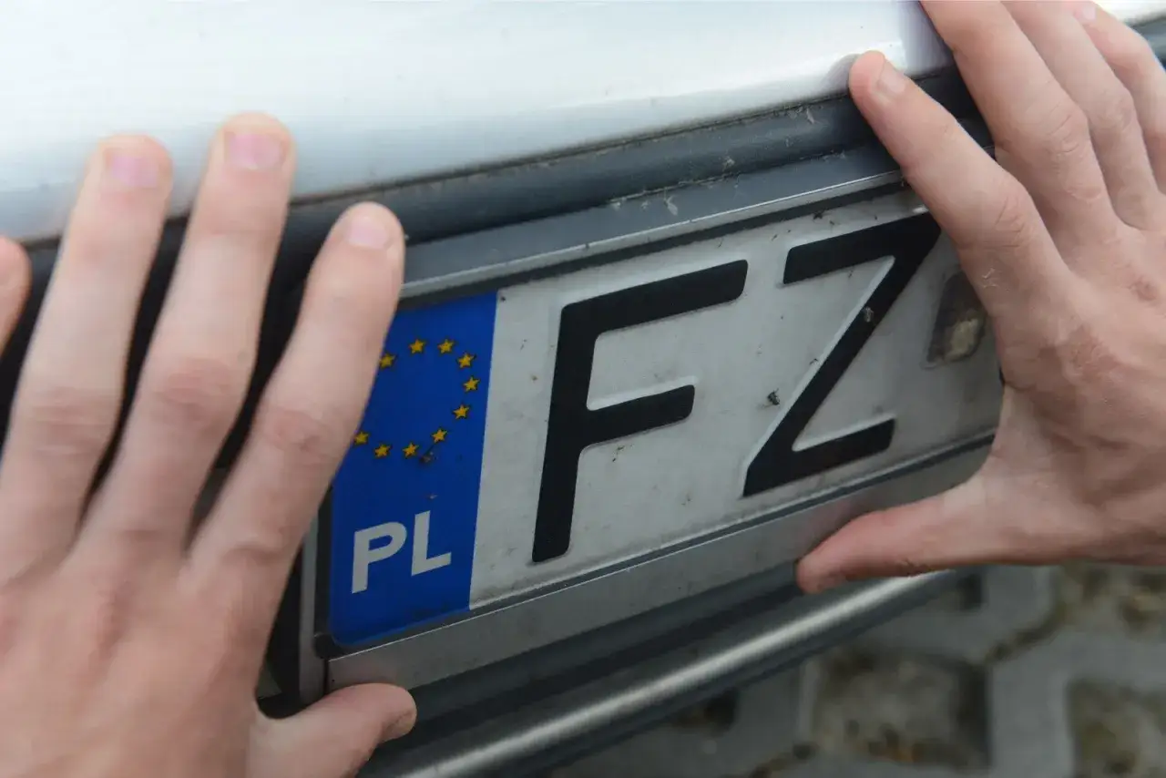 Dłonie trzymają tablicę rejestracyjną z oznaczeniem FZ i symbolem Unii Europejskiej.