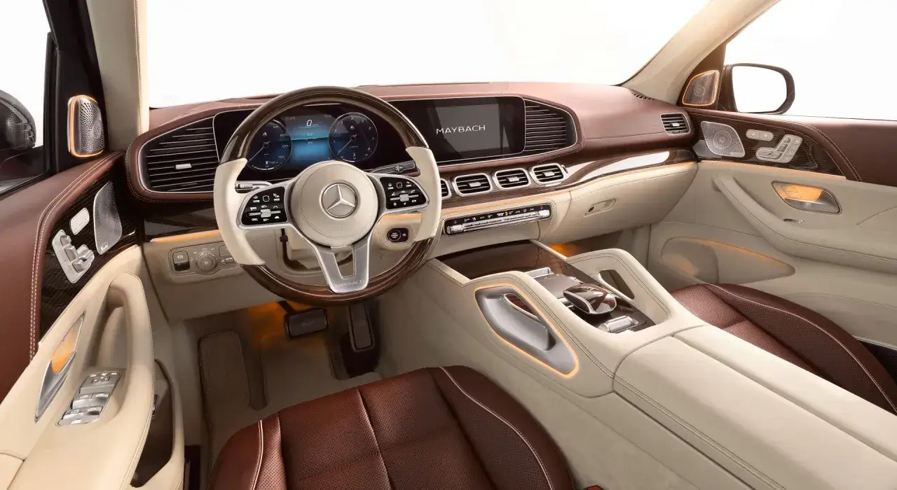 Luksusowe wnętrze Mercedes GLS Maybach z brązową i beżową skórą, drewnianymi wstawkami i ambientowym oświetleniem.