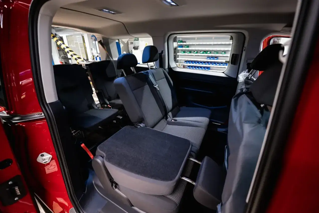 Wnętrze czerwonego caddy 3 z rzędami siedzeń i oknem z półkami.