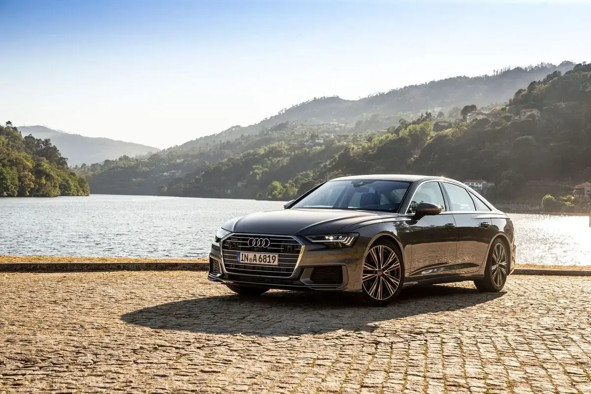 Elegancki Audi A6, z jego imponującymi wymiarami, parkuje nad jeziorem w słoneczny dzień.