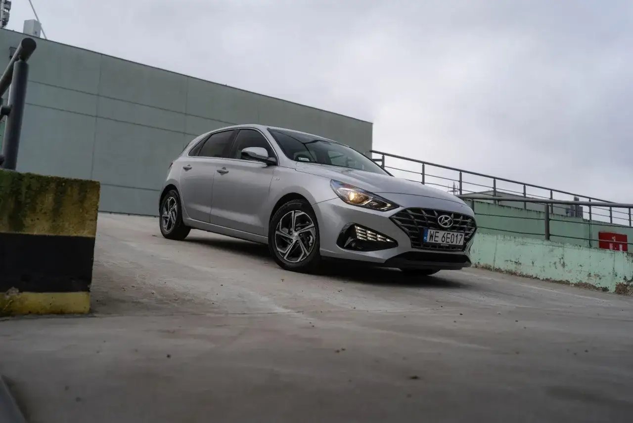 Srebrny Hyundai i30 hatchback na betonowym placu, z szarym budynkiem w tle.