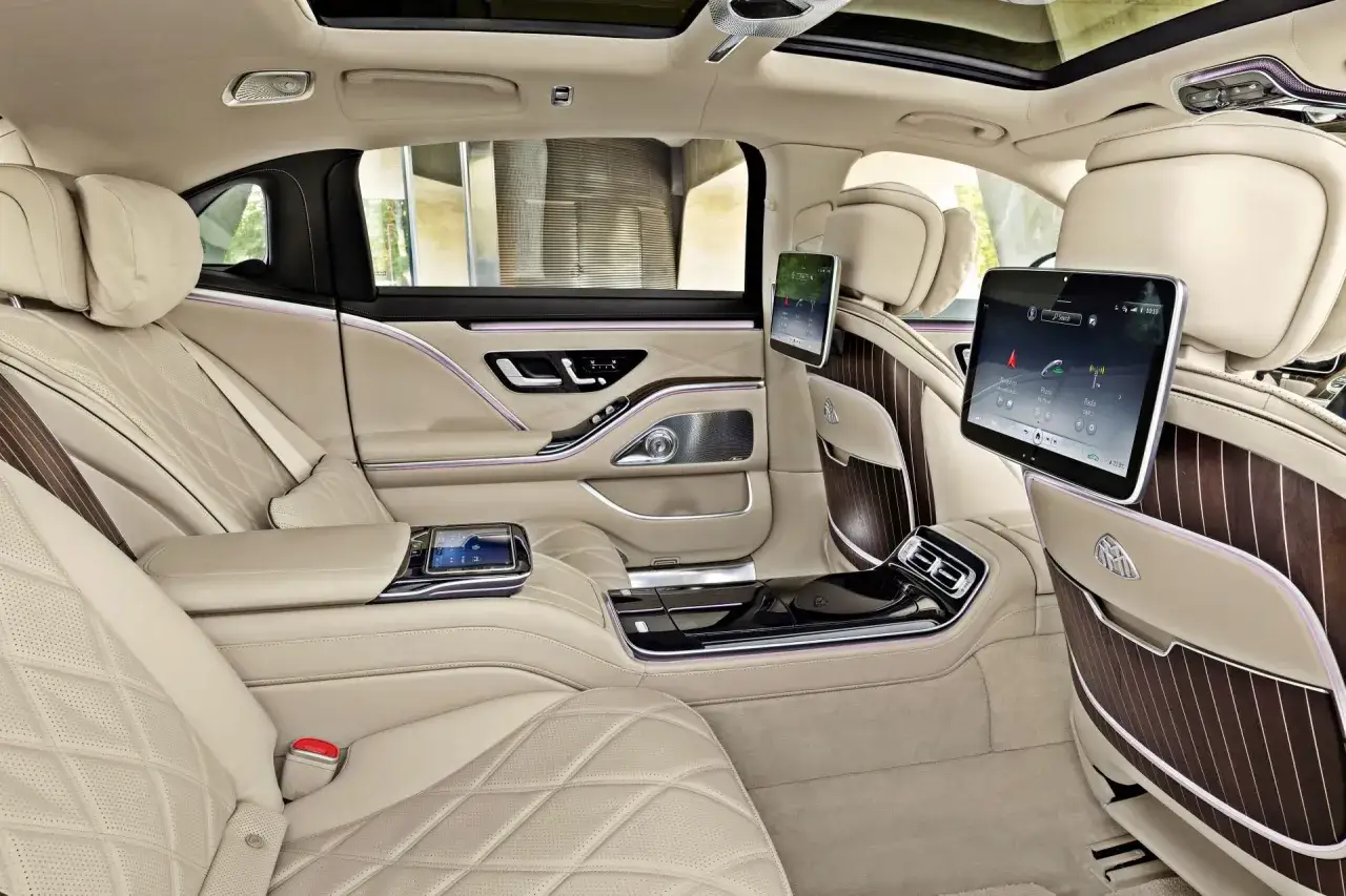 Luksusowe wnętrze Maybach S580 z beżową skórzaną tapicerką, ekranami dla pasażerów i ambientowym oświetleniem.