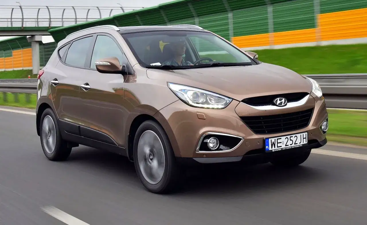Brązowy Hyundai ix35 na drodze. Kierowca w okularach, za nim zielono-żółte ekrany dźwiękochłonne.