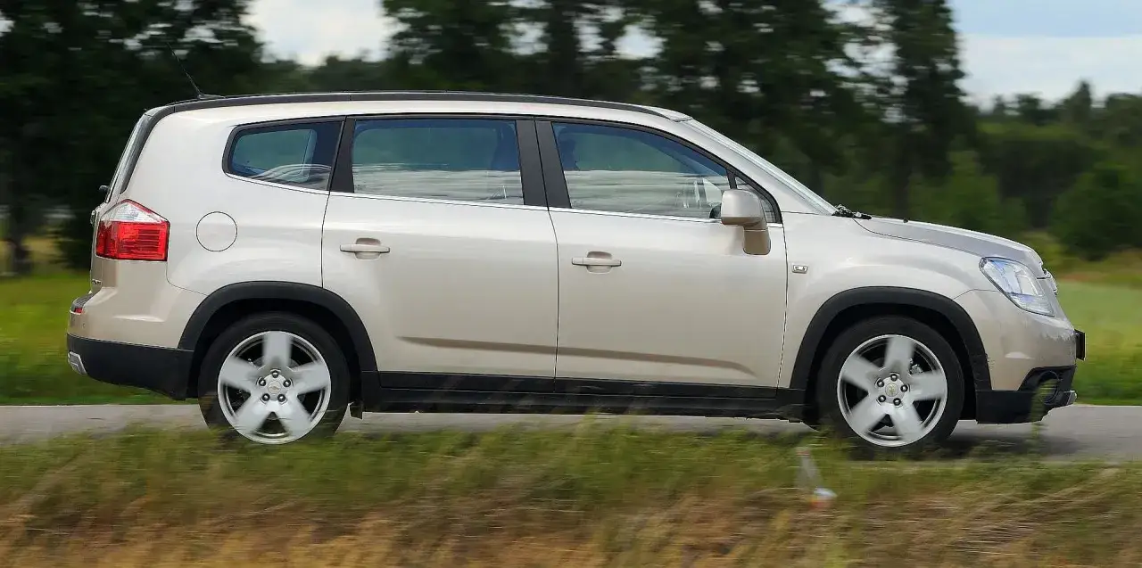 Złoty Chevrolet Orlando 1.8 benzyna w ruchu, z rozmytym tłem drzew i trawy.