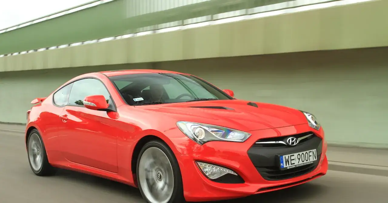 Czerwony Hyundai Genesis Coupe 3.8 V6 pędzi pod zieloną estakadą.