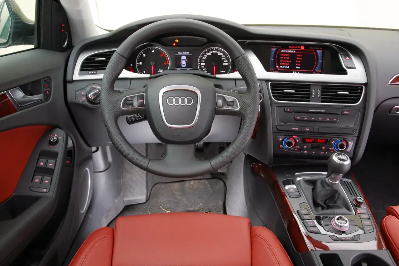 Wnętrze Audi A4 B8 z czerwonymi skórzanymi fotelami. Kierownica, deska rozdzielcza i ekran multimediów. Wiele osób szuka audi a4 b8 opinie przed zakupem.