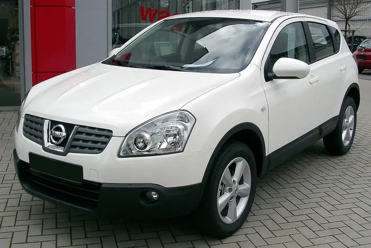 Biały Nissan Qashqai 1.6 benzyna stoi na parkingu przed salonem samochodowym.