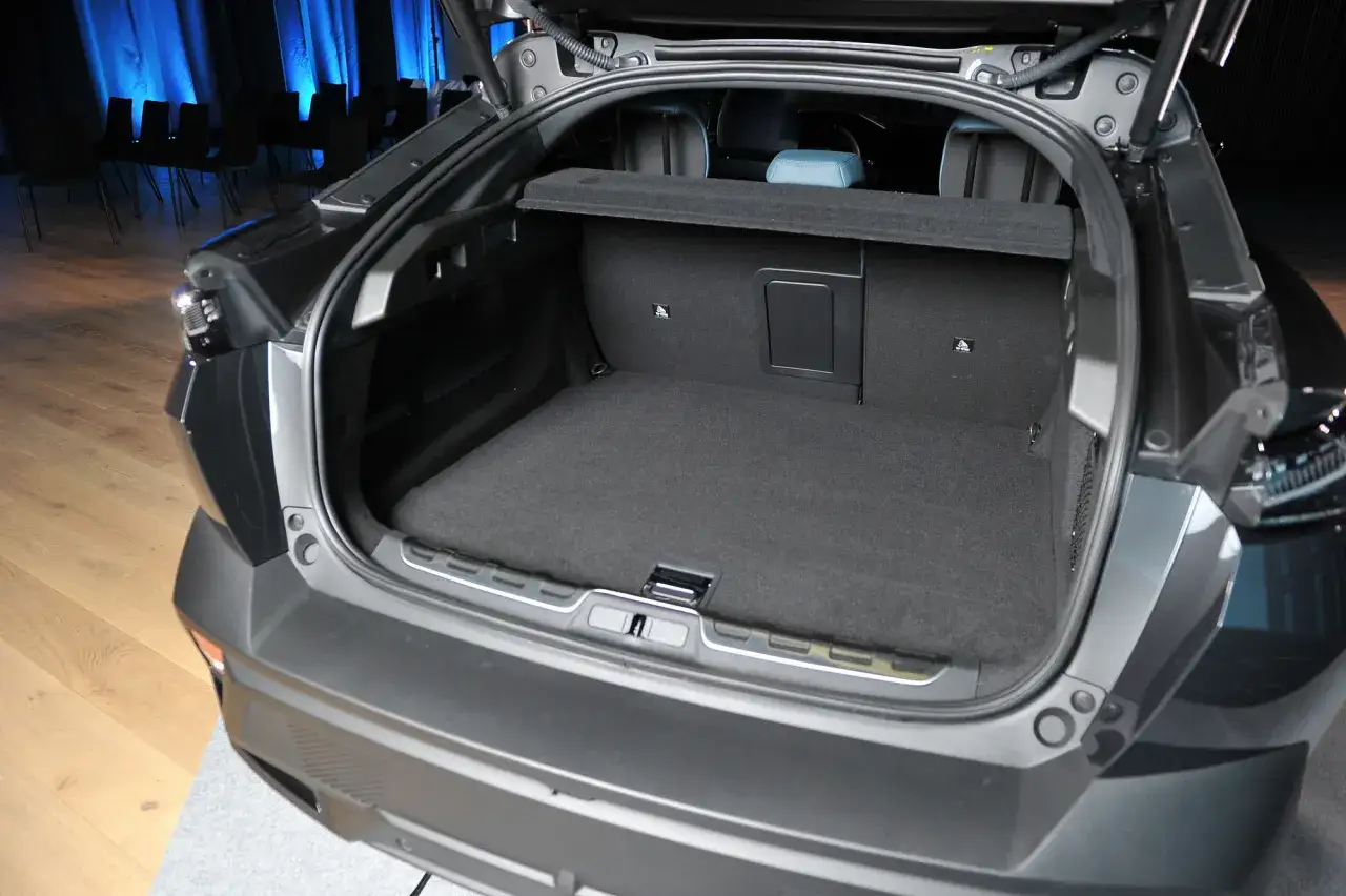 Otwarty bagażnik Peugeot 408 Hybrid. Wnętrze wyłożone czarną wykładziną, widoczne tylne siedzenia.