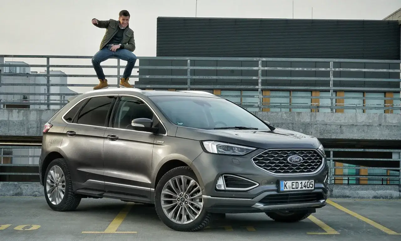 Mężczyzna na dachu Forda Edge, który imponuje swoimi wymiarami. Stylowy SUV na tle nowoczesnej architektury.