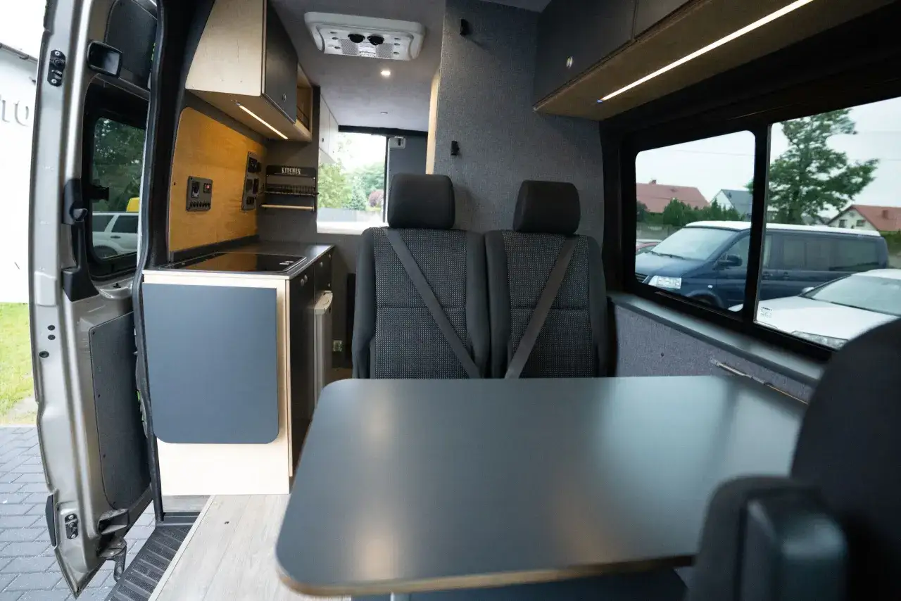 Wnętrze kampera na bazie Mercedesa Sprintera: kuchnia, dwa fotele, stół. Gotowy na podróż!