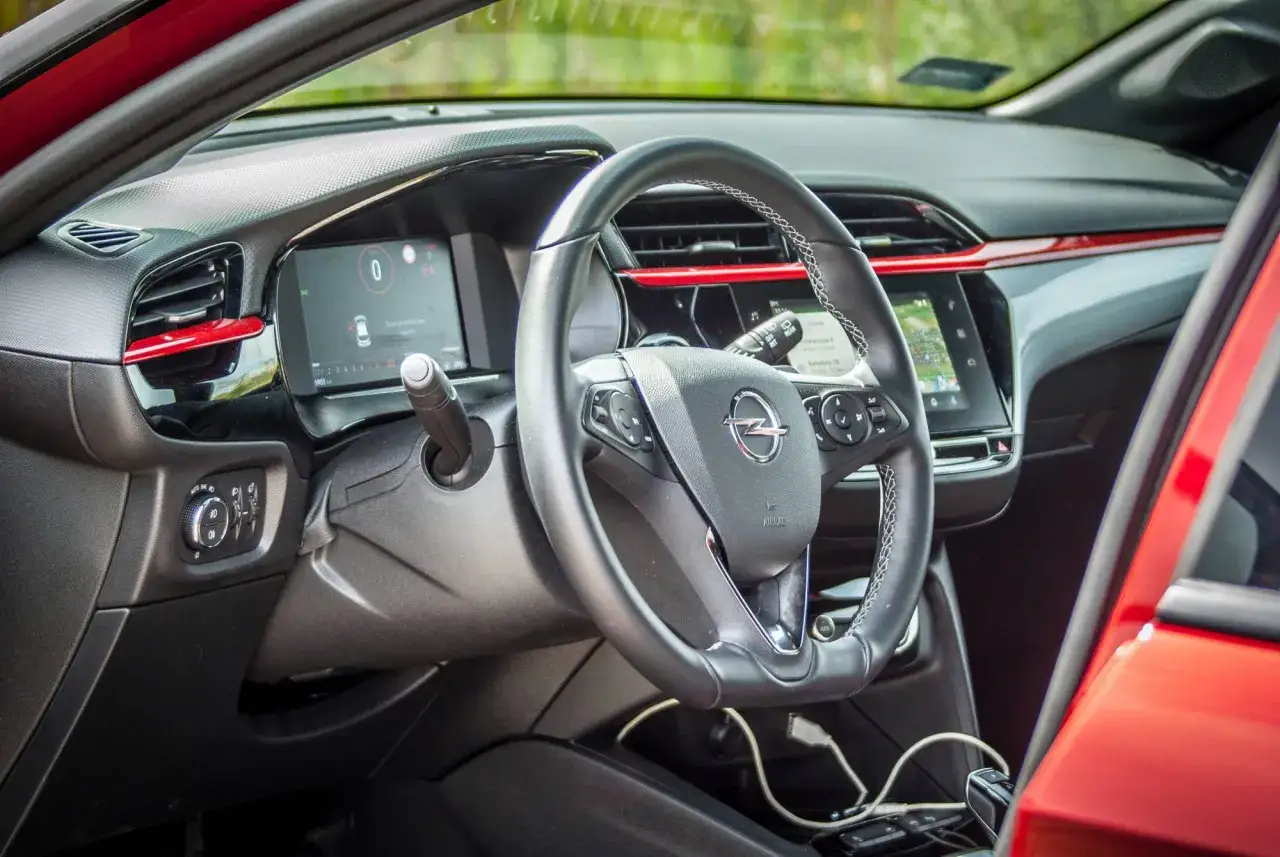 Wnętrze nowoczesnego Opla Corsy 2022 z cyfrowymi zegarami i ekranem multimedialnym. Czerwone akcenty dodają sportowego charakteru.