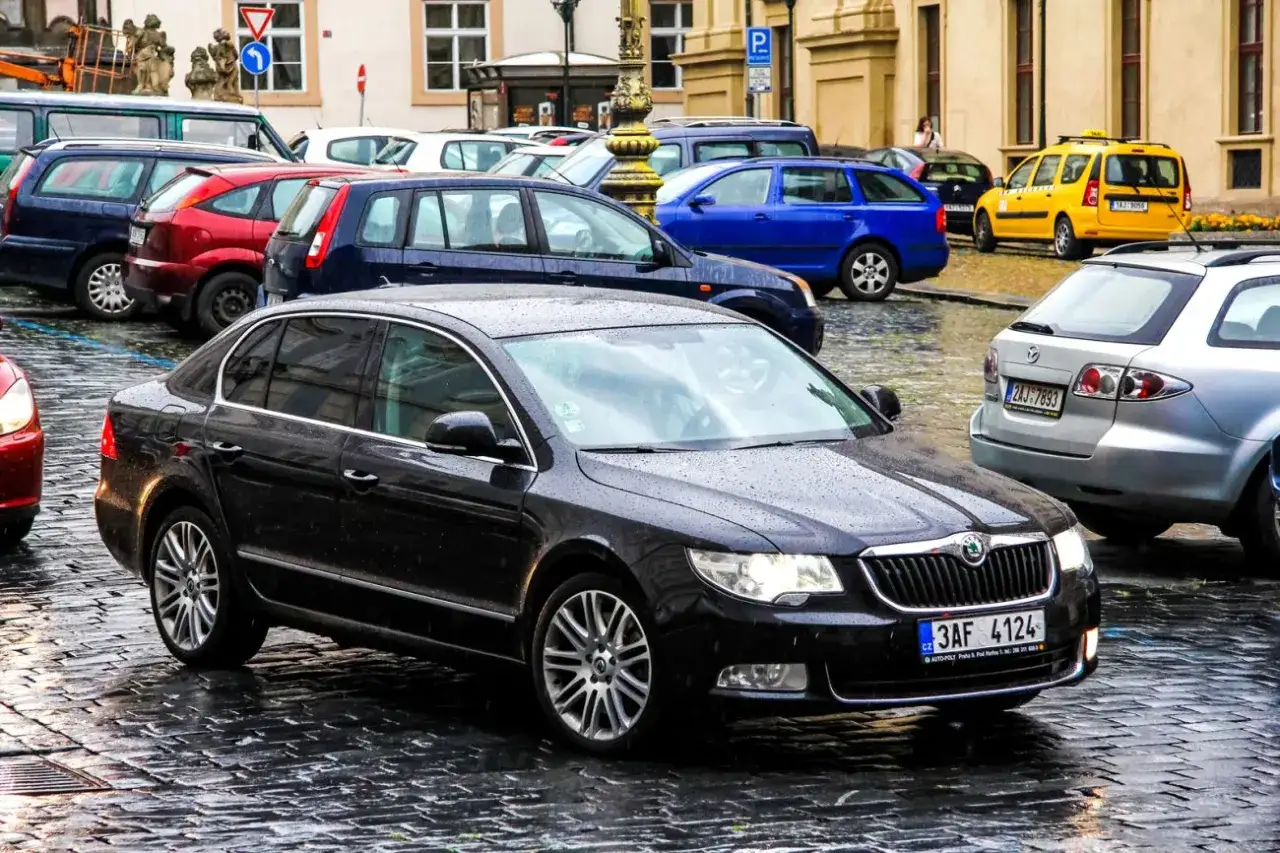 Czarny liftback Skoda na mokrej, brukowanej ulicy w mieście.