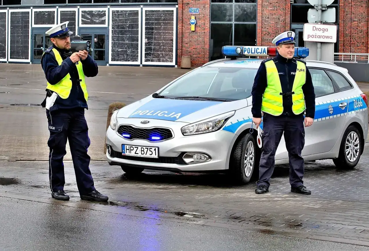 Policjanci z radarem mierzą prędkość. Jeden celuje, drugi stoi obok radiowozu. Przekroczenie prędkości o 20 km/h to mandat.