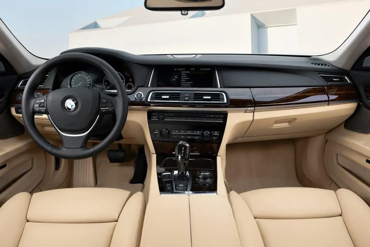 Wnętrze BMW 7 F01: skórzana tapicerka, drewniane wykończenia, kierownica i ekran multimedialny.