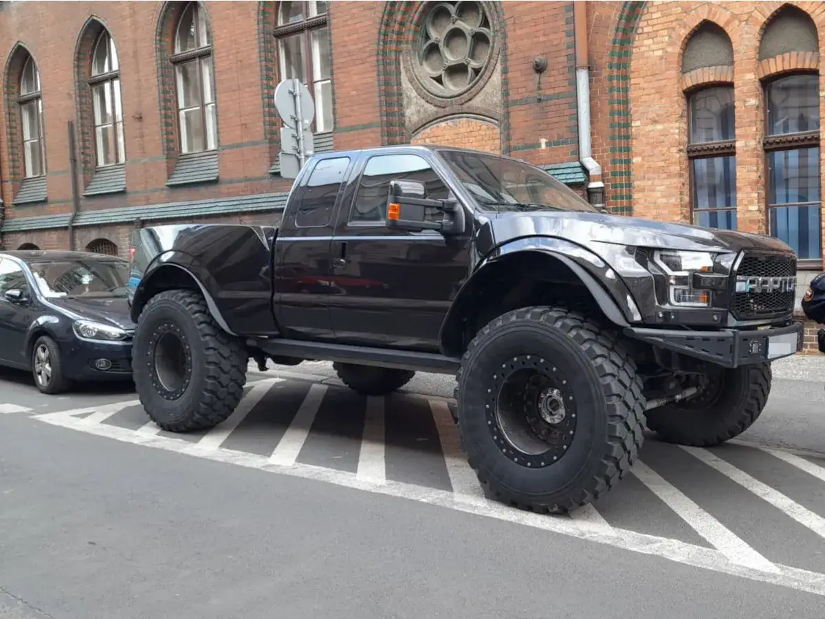 Czarny Ford F250 z ogromnymi oponami, gotowy na terenowe wyzwania, parkuje obok zwykłego samochodu.