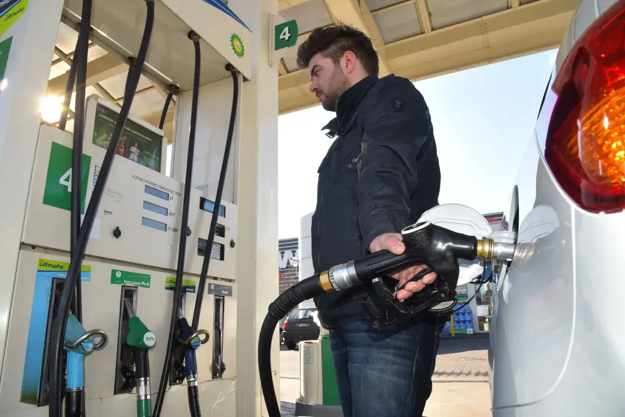 Mężczyzna tankuje swoje audi 90 na stacji BP. Słońce odbija się w lakierze samochodu.