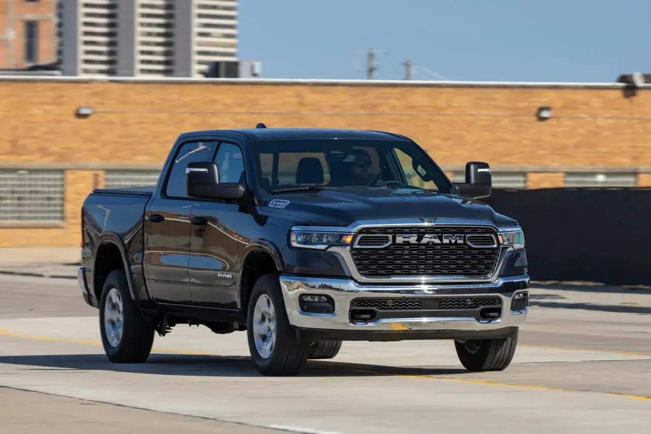 Czarny Dodge Ram 1500 5.7 Hemi z chromowanymi elementami jedzie po drodze, za nim ceglany budynek.