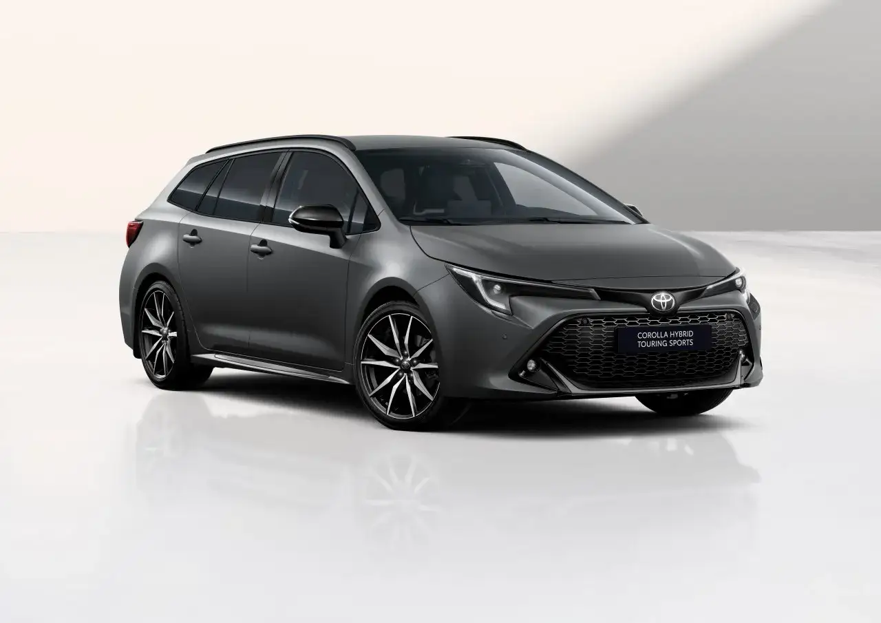 Szary kombi Toyota Corolla Hybrid Touring Sports z czarnymi felgami stoi na białym tle, odbijając się w gładkiej powierzchni.