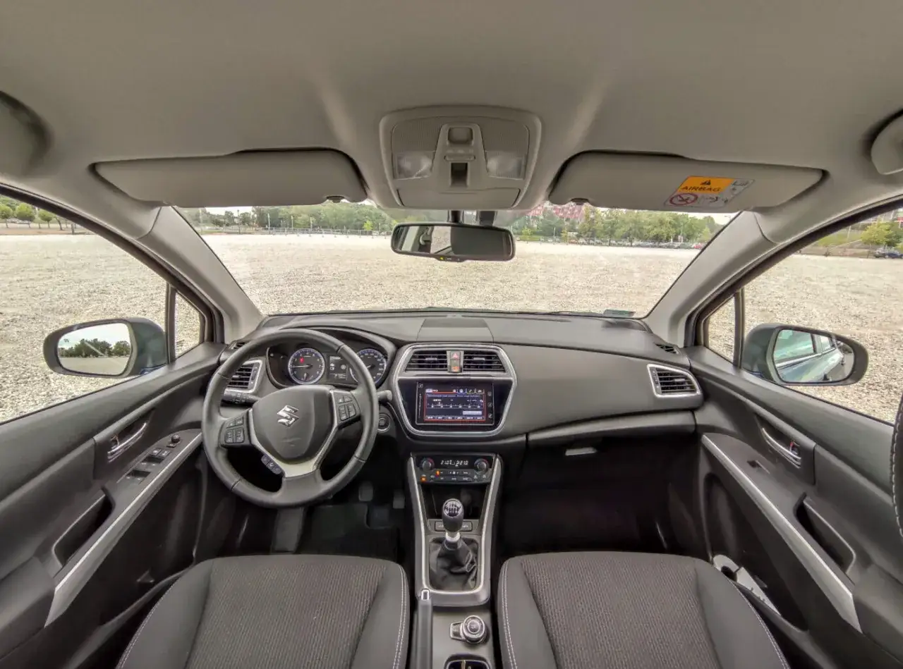 Wnętrze Suzuki SX4 S-Cross. Widok na deskę rozdzielczą, kierownicę i fotele. Wady tego modelu mogą dotyczyć np. jakości materiałów.