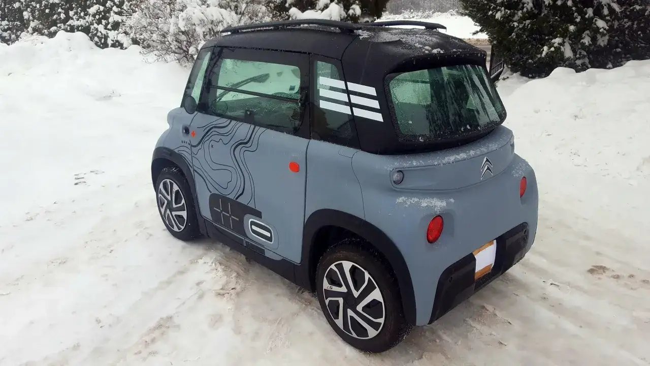 Szary Citroen Ami z czarnym dachem i białymi pasami na tylnej szybie, zaparkowany na śniegu. Sprawdź atrakcyjną citroen ami cena!