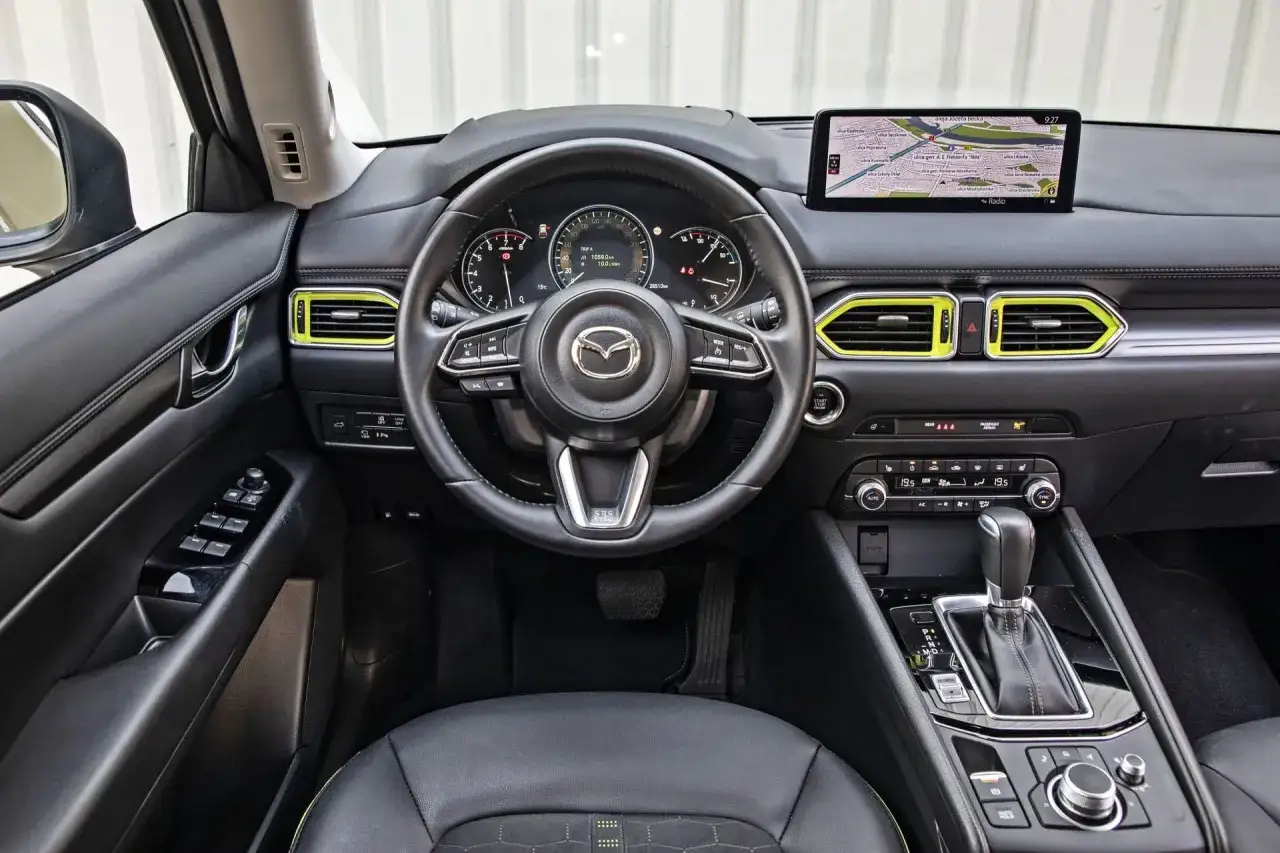 Wnętrze Mazdy CX-5 z żółtymi akcentami. Kierownica, nawigacja i panel klimatyzacji. Sprawdź mazda cx-5 cena!