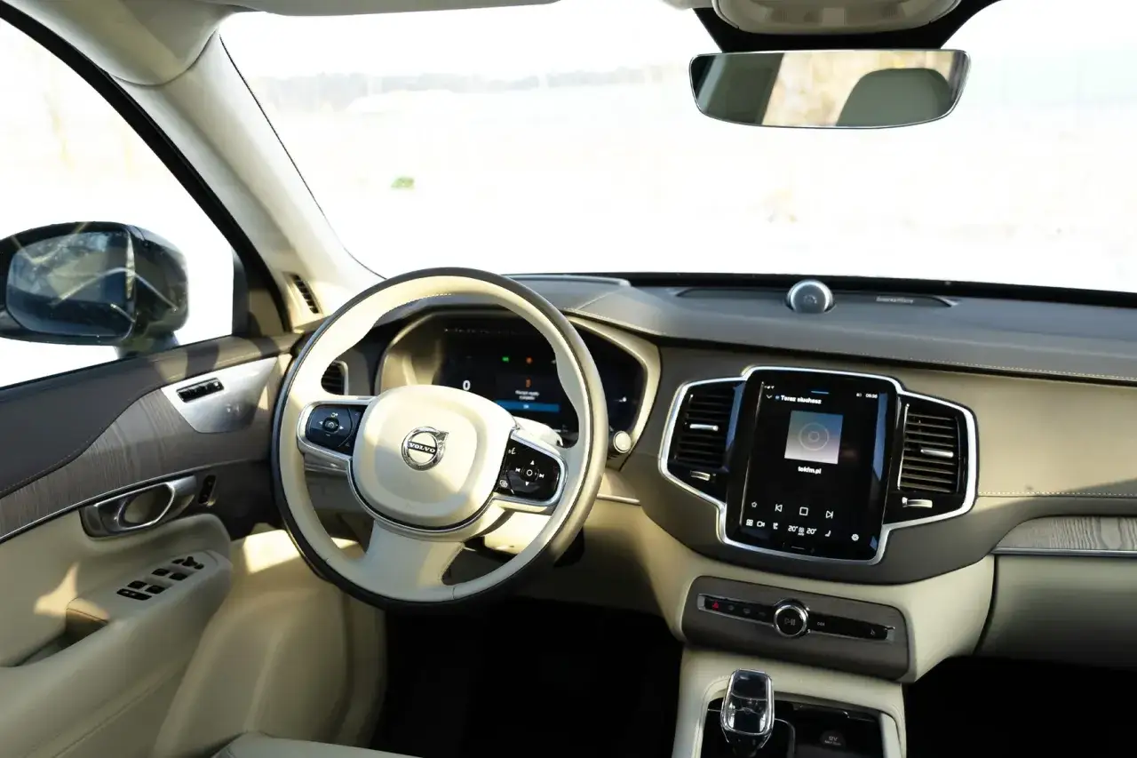 Wnętrze Volvo XC90 2020 z jasną tapicerką, drewnianymi wstawkami i dużym ekranem multimedialnym.