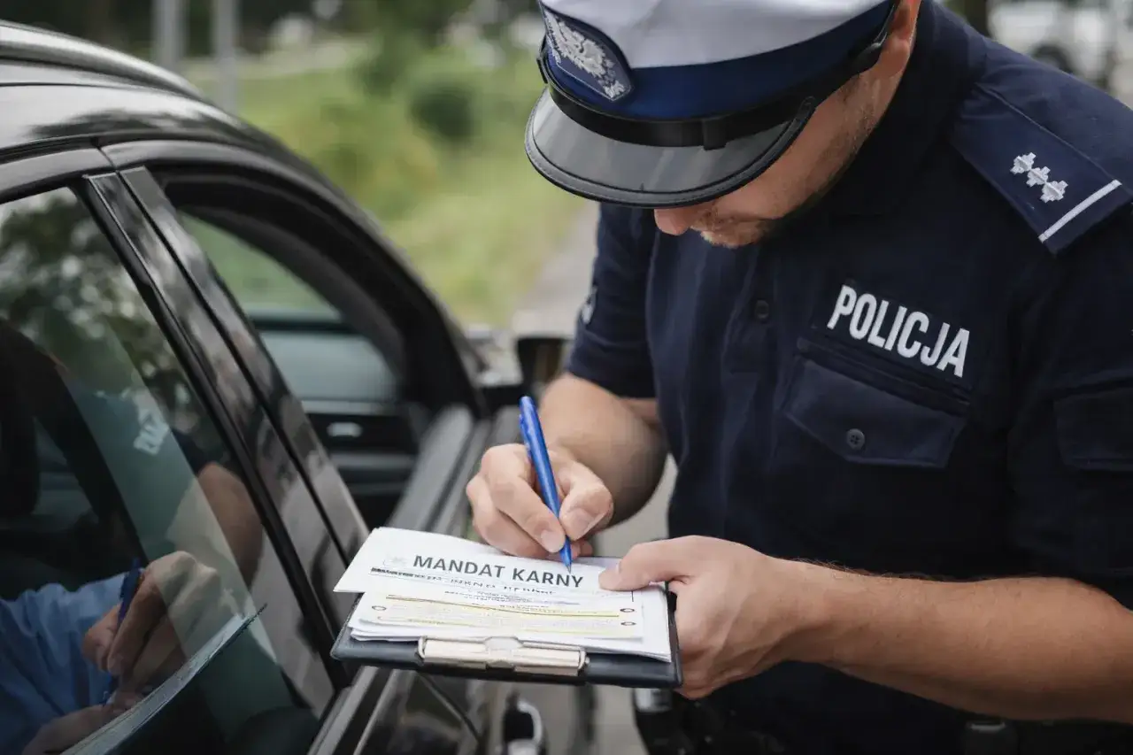 Policjant wypisuje mandat karny kierowcy. To już jego kolejny mandat, recydywa mandatowa.
