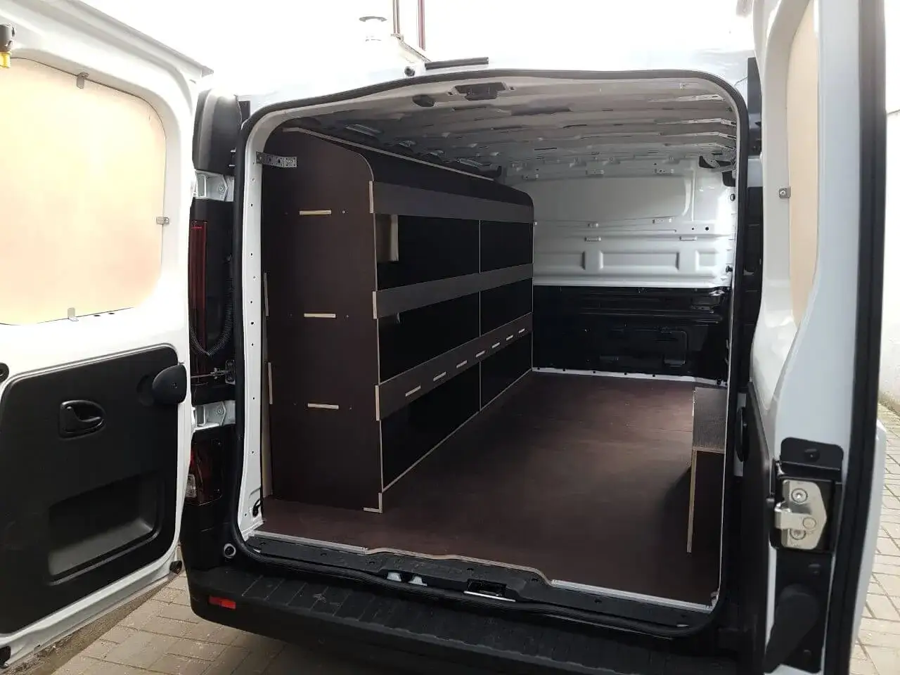 Wnętrze białego Renault Trafic 3 z zabudową warsztatową. Półki i przegrody z ciemnej sklejki.