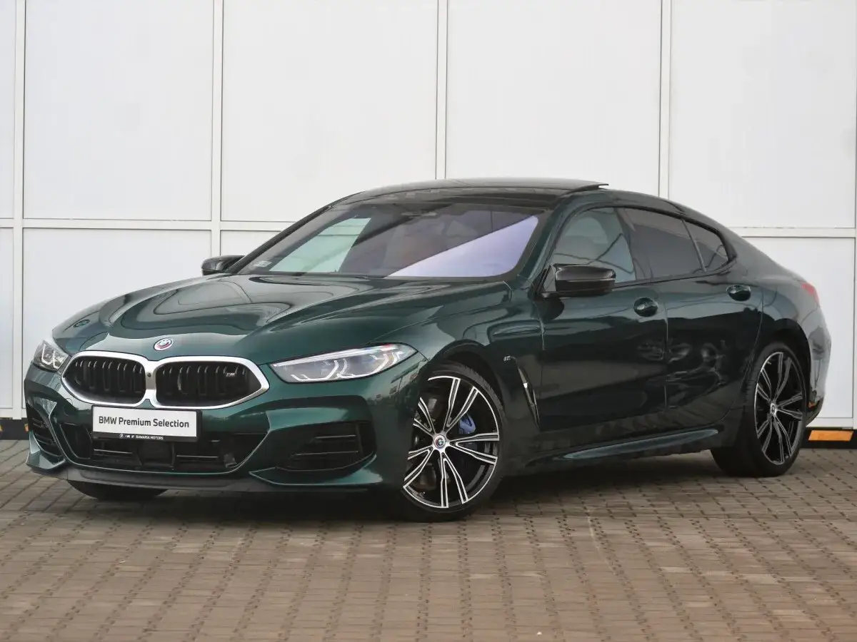 Eleganckie, ciemnozielone BMW 840d z czarnymi felgami i przyciemnianymi szybami, zaparkowane przed budynkiem.