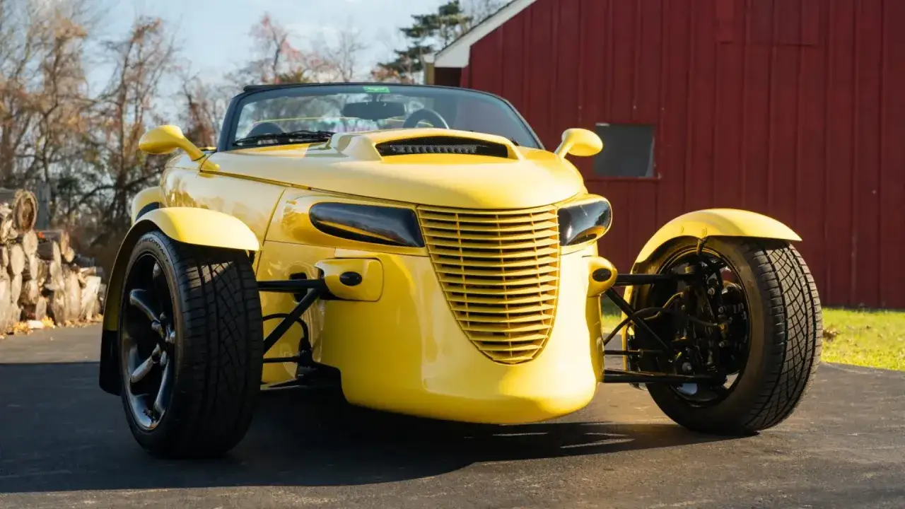 Żółty Plymouth Prowler z otwartym dachem, zaparkowany przed czerwoną stodołą.