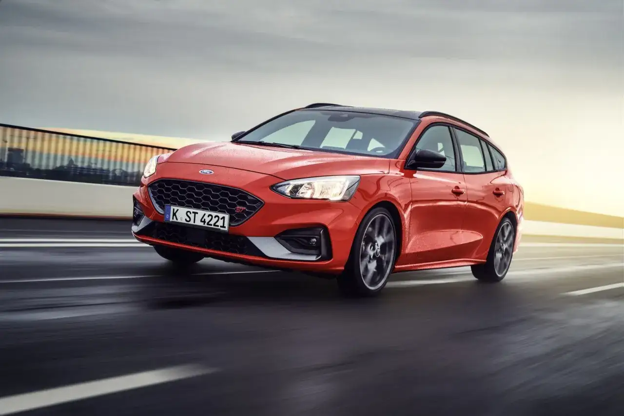 Czerwony Ford Focus kombi ST pędzi po drodze, z rozmytym tłem i światłami w tle.