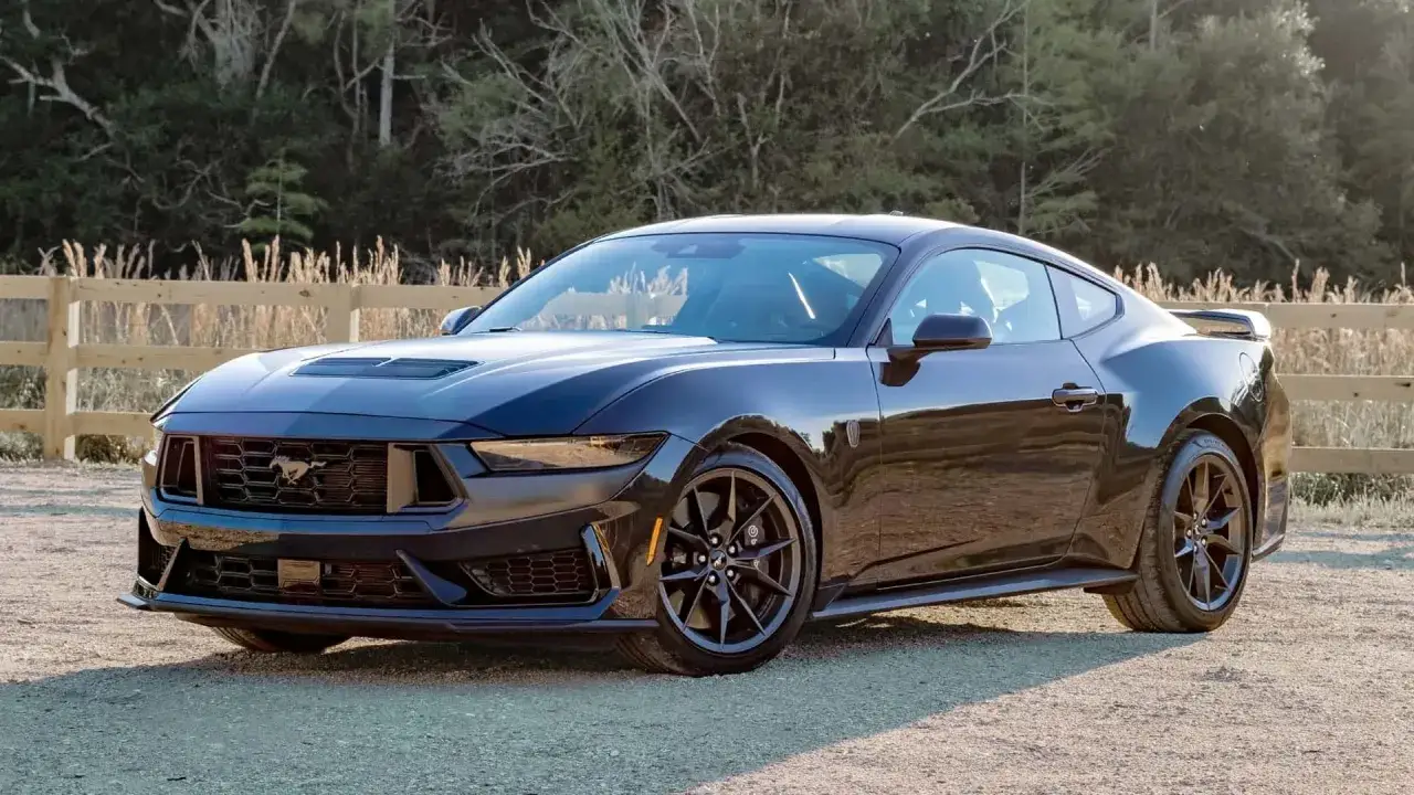 Czarny Ford Mustang na tle drewnianego płotu. Sprawdź aktualną mustang cena i dowiedz się, jak stać się jego właścicielem.