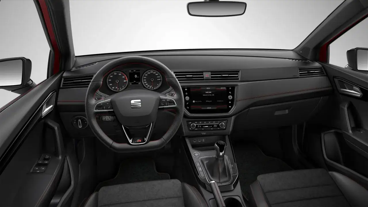 Wnętrze Seata Arona z czerwonymi przeszyciami. Kierownica, deska rozdzielcza i ekran multimedialny. Wiele osób szuka seat arona opinie, a to wnętrze pokazuje nowoczesność i sportowy charakter.