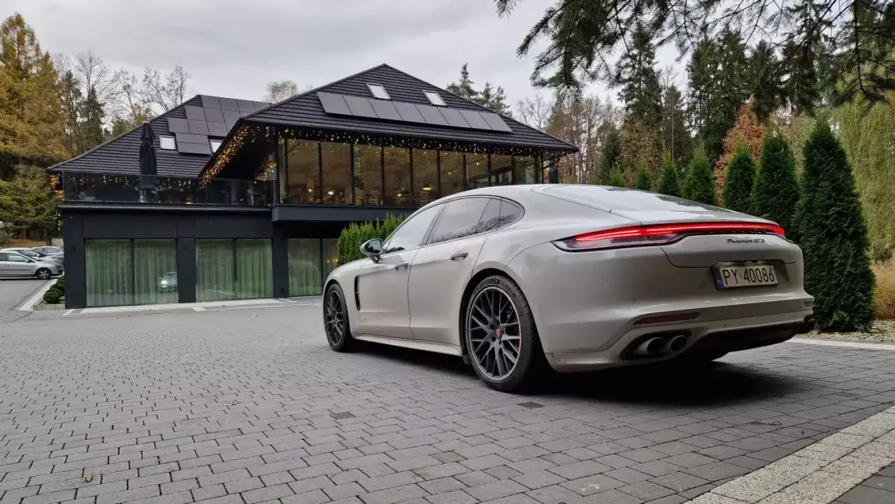 Białe Porsche Panamera GTS przed nowoczesnym budynkiem z panelami słonecznymi. Idealny wybór dla firm ceniących leasing operacyjny i prestiż.
