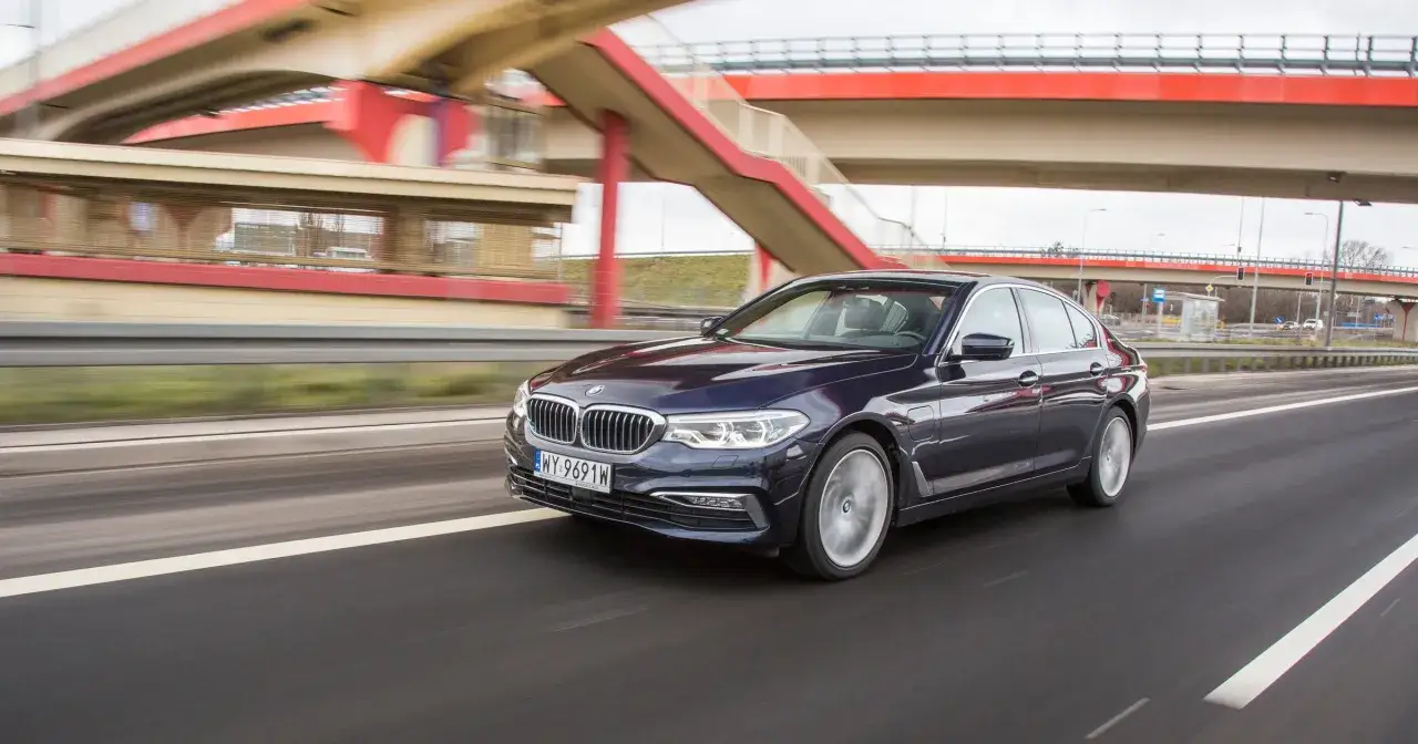Ciemnogranatowe BMW 530 jedzie autostradą pod czerwonym wiaduktem.
