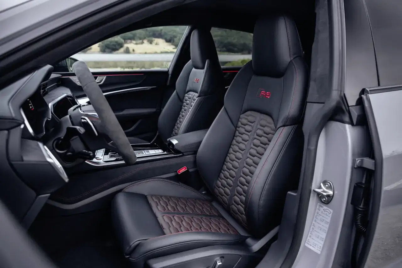Wnętrze Audi RS7 z czarną skórzaną tapicerką i czerwonymi przeszyciami. Sportowe fotele z logo RS. Zastanawiasz się nad audi rs7 cena?