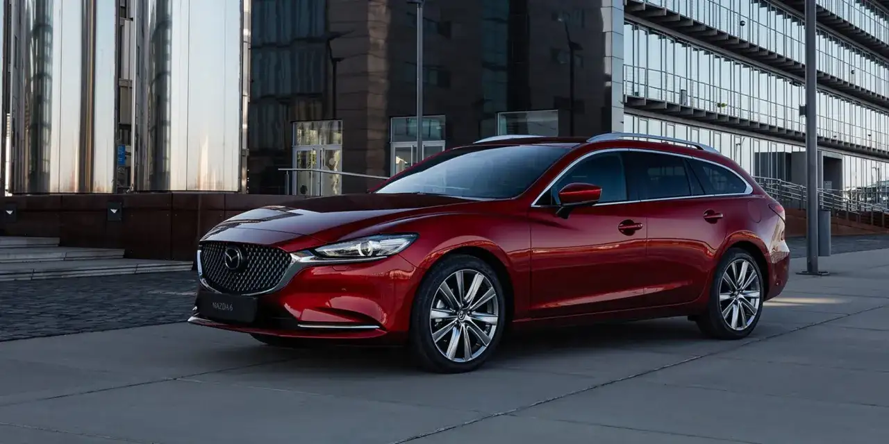 Czerwona Mazda 6 kombi na tle nowoczesnego budynku. Sprawdź jej wymiary i pojemność bagażnika.