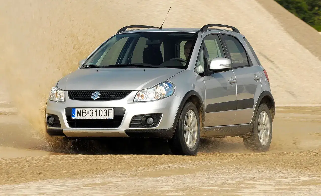 Srebrny Suzuki SX4 pokonuje piaszczysty teren, wzbijając tumany kurzu. Wiele pozytywnych suzuki sx4 opinie potwierdza jego wszechstronność.