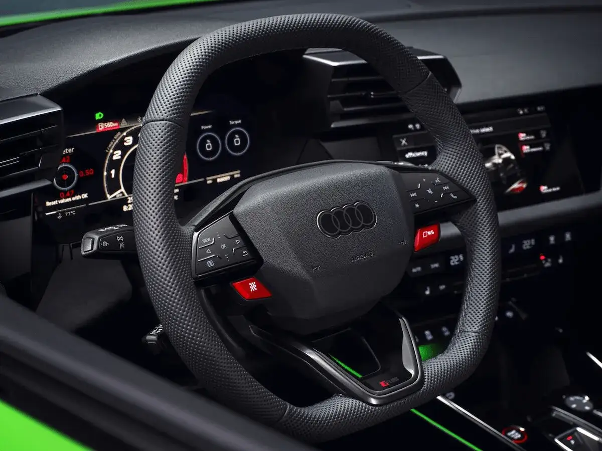 Wnętrze Audi RS3 Sedan: perforowana kierownica, cyfrowe zegary i czerwony przycisk RS.