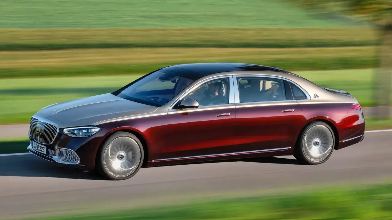 Elegancki, dwukolorowy Mercedes-Maybach sunie po drodze, otoczony rozmytym krajobrazem pól.