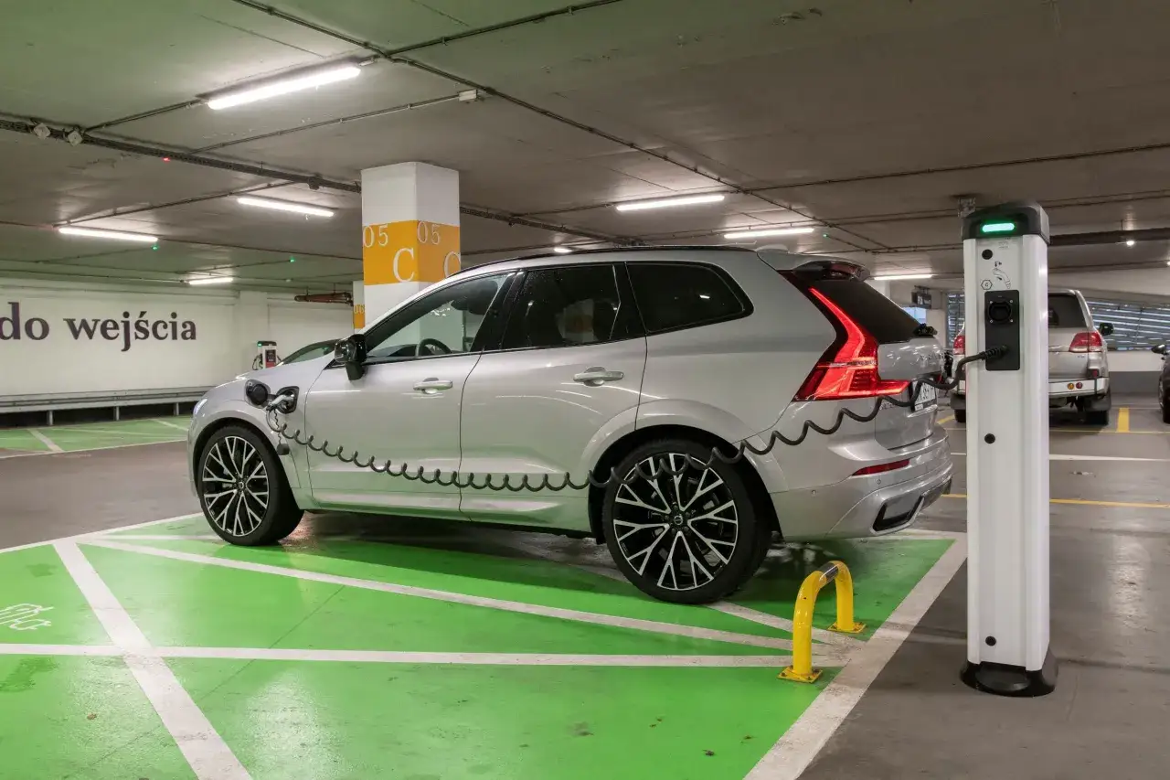 Srebrne Volvo XC60 T8 na zielonym polu ładowania w podziemnym parkingu, podłączone do stacji ładowania.