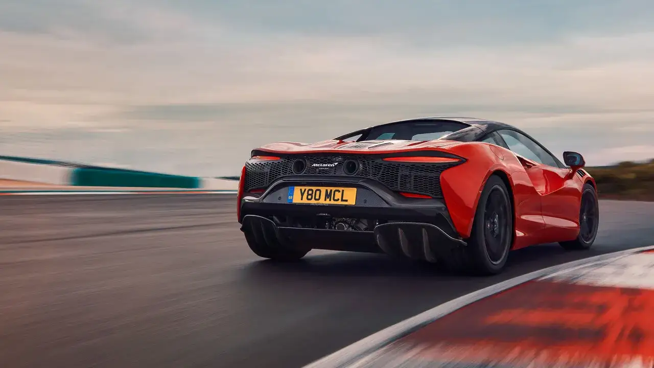 Pomarańczowy McLaren pędzi po torze wyścigowym. Jego cena jest wysoka, ale wrażenia bezcenne.
