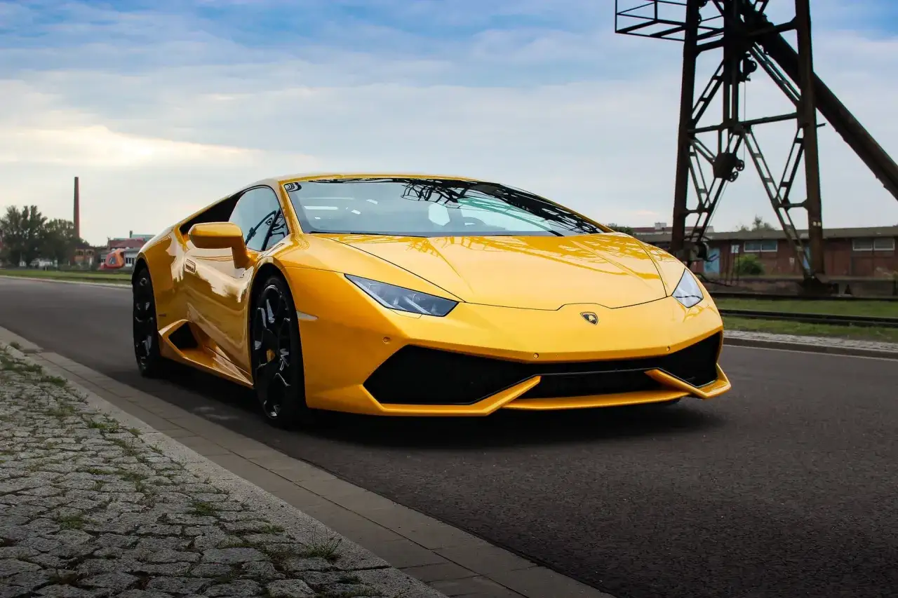 Żółty Lamborghini Huracan na drodze, obok torów kolejowych. Marzenie o tym aucie i jego cena są kuszące.